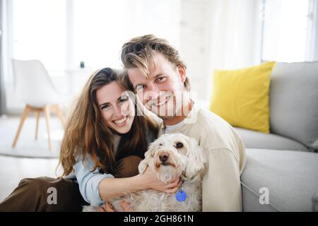 Glückliches junges Paar in der Liebe mit Hund drinnen zu Hause, Blick auf die Kamera. Stockfoto
