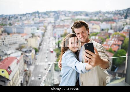 Glückliches junges Paar in der Liebe, das zu Hause draußen auf dem Balkon steht und Selfie mit dem Smartphone macht. Stockfoto