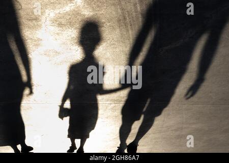 Verschwommene Schattensilhouette eines kleinen Mädchens, das an einem Sommertag Hand in Hand mit einem Vater auf einer Promenade geht, in Sepia schwarz und weiß Stockfoto