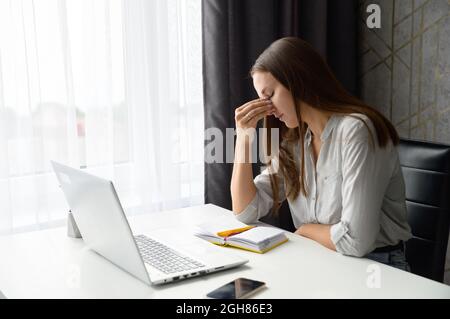 Aufgeregt gestresst besorgt Frau sitzt vor dem Laptop, hält Brücke der Nase, weibliche Büroangestellte fühlt sich müde, haben Kopfschmerzen oder Migräne. Überarbeiteter Begriff Stockfoto