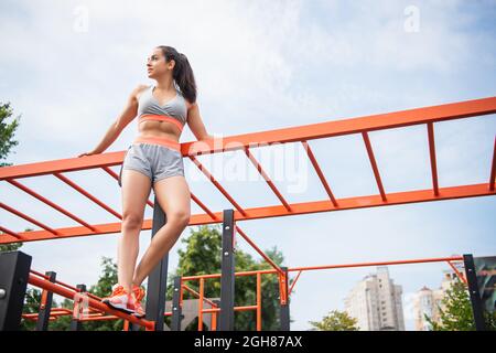 Niedrige Ansicht der jungen Sportlerin, die in der Nähe einer orangefarbenen horizontalen Leiter draußen steht Stockfoto