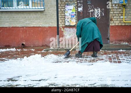 Eine alte Oma Yard Mann räumt den Schnee am Eingang. Stockfoto