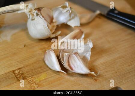 Frisch geschnittene Knoblauchzehen, allium sativum, wie sie aus der Glühbirne extrahiert wurden, werden in einer heimischen Küche auf einem hölzernen Brotbrett geschnitten Stockfoto