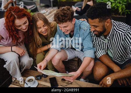 Draufsicht auf eine Gruppe von glücklichen jungen Menschen, die auf einem Stadtausflug im Café im Freien sitzen, auf der Karte. Stockfoto