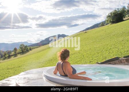 21. August 2021: Frau in einem Badeanzug von hinten entspannt sich in einem Whirlpool im Freien mit einer grünen Wiese Stockfoto