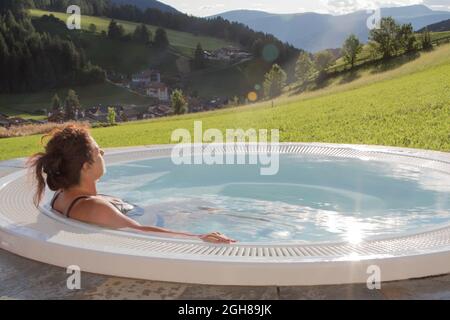 21. August 2021: Frau in einem Badeanzug von hinten entspannt sich in einem Whirlpool im Freien mit einer grünen Wiese Stockfoto