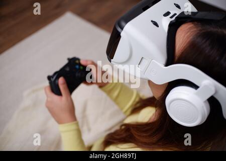 Junge asiatische Frau, die im Wohnzimmer Videospiele mit einer Virtual-Reality-Brille spielt. Stockfoto