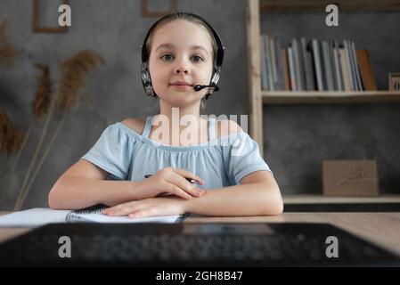 Porträt eines glücklichen kleinen Studenten, der zu Hause studiert. Lächelndes kleines Mädchen, das im Wohnzimmer Unterricht genießt. Smart Kind Schulmädchen schaut auf die gekommen Stockfoto