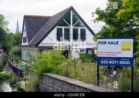 Leeres und leerstehendes Pub zum Verkauf mit Immobilienmaklern im Vordergrund und überwucherter Terrassenbereich Stockfoto