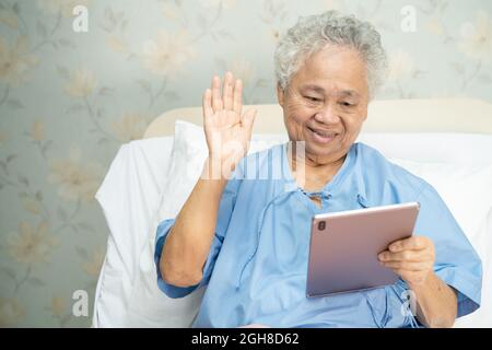 Asiatische ältere oder ältere alte Dame, die digitale Tablets für Videoanruf verwendet; Konzept der sozialen Distanzierung. Stockfoto