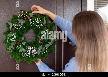 Frau hängt einen Weihnachtskranz an der Eingangstür Stockfoto