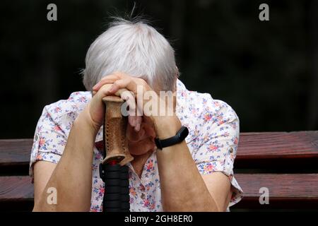 Ältere Frau, die mit dem Kopf nach unten auf Spazierstöcken auf einer Bank sitzt. Krankheit und Müdigkeit, gesunder Lebensstil im Alter, Leben im Ruhestand Stockfoto