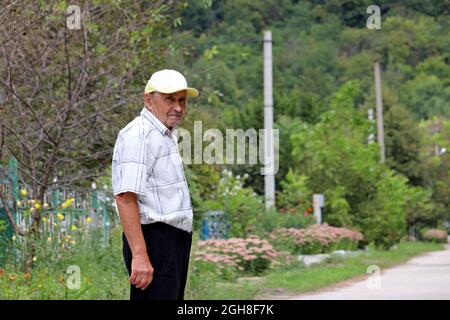 Älterer Mann, der auf einer ländlichen Straße steht. Konzept des Lebens im Dorf, Alter Stockfoto