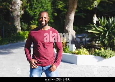 Porträt eines afroamerikanischen Mannes, der lächelt und die Kamera im sonnigen Garten anschaut Stockfoto