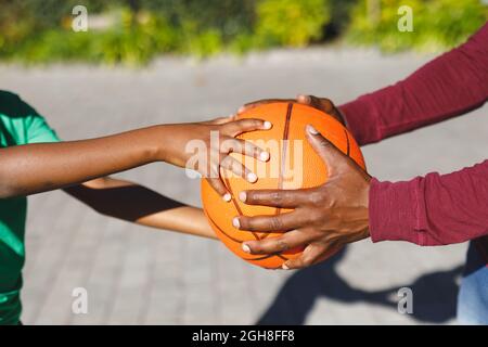 Mittelteil von afroamerikanischem Vater und Sohn, der Basketball im Garten hält Stockfoto