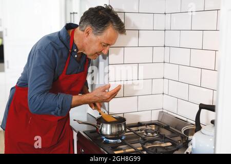 Glücklicher älterer kaukasischer Mann mit Schürze beim Kochen in der Küche Stockfoto