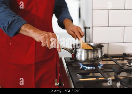 Mittelteil eines älteren kaukasischen Mannes mit Schürze beim Kochen in der Küche Stockfoto