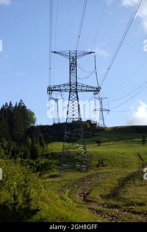 Hochspannungs-elektrische Türme und Linien mit blauem Himmel und grüner Wiese. Eleetricity Türme auf einem grünen Feld. Hochspannungsübertragungsleitungen. Stockfoto