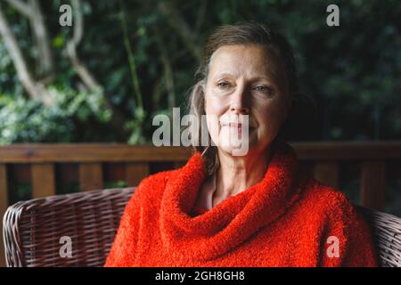 Glückliche ältere kaukasische Frau, die im Garten auf einem Stuhl sitzt Stockfoto