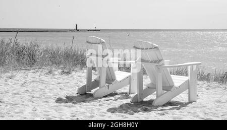 Leere Adirondack-Rasenstühle im Freien entlang der Uferpromenade und dem Strand Stockfoto