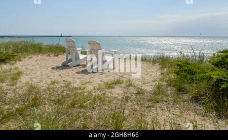 Leere Adirondack-Rasenstühle im Freien entlang der Uferpromenade und dem Strand Stockfoto