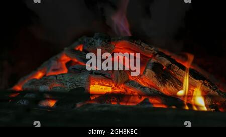 Nahaufnahme des Feuers in Innenräumen als Hintergrund. Grill Lagerfeuer in der Nacht. Schwaches Licht mit selektivem Fokus. Textur von Feuerflammen mit Kohlen und Brennholz Stockfoto