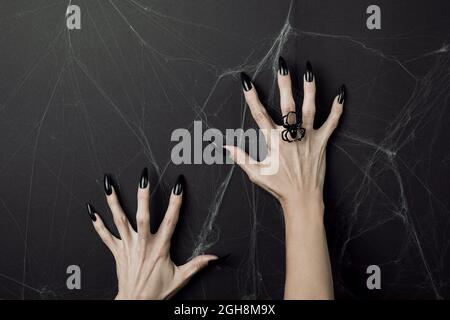 Hände mit langen schwarzen Nägeln und Spinnenring auf schwarzem Hintergrund mit Spinnweben. Happy Halloween Feiertagskonzept. Stockfoto