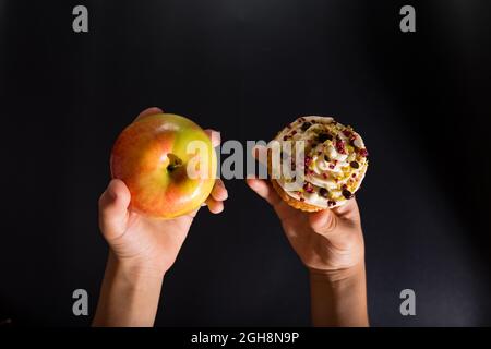 Das Kind wählt zwischen Süßigkeiten und Früchten, Nahaufnahme auf schwarzem Hintergrund. Stockfoto