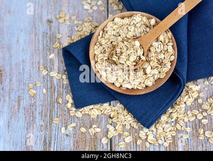 Haferflocken ungekocht in Holzschüssel mit Löffel auf rustikalem Tisch. Konzept der gesunden Ernährung Stockfoto