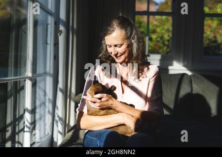 Glückliche ältere kaukasische Frau im Schlafzimmer, die ihre Katze in der Hand hält Stockfoto