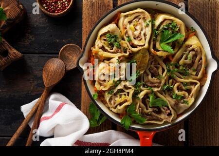 Fleischteig rollt mit Fleisch oder faulen Knödeln in einer gusseisernen Pfanne auf einem alten rustikalen Holzhintergrund. Draufsicht Stockfoto