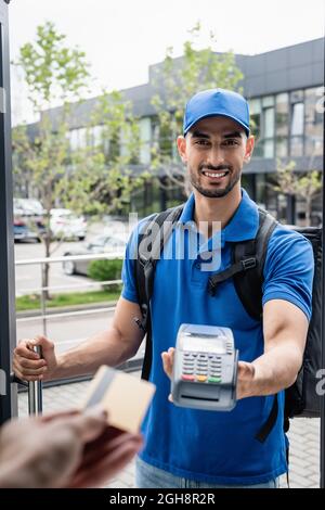 Lächelnder muslimischer Überlieferer, der das Terminal in der Nähe des Kunden mit Kreditkarte hält Stockfoto