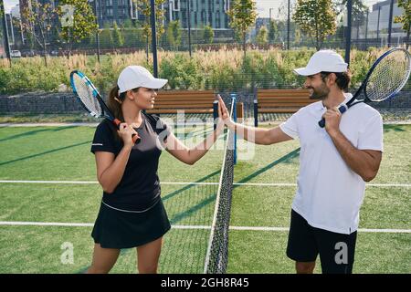 Tennisspieler, die vor dem Spiel in der Nähe des Tennisnetzes Handschütteln. Mann und Frau spielen Tennis eins zu eins Stockfoto