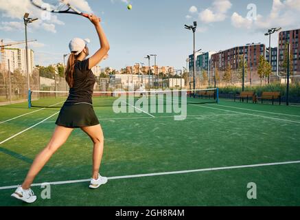 Die Tennisspielerin spielt mit ihrem männlichen Partner auf einem Rasenplatz in städtischer Umgebung Ball. Tennisspielerin mit Tennisschläger und Stockfoto
