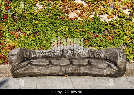 Sitzbank aus altem Baumstamm, geschnitzt im Jahre 2007 mit Aufschrift 'Benevent l'Abbaye MMVII' - Bénévent-l'Abbaye, Creuse (23), Nouvelle-Aquitaine, Frankreich. Stockfoto