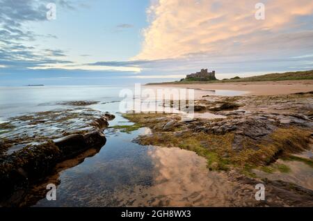 Bamburgh Castle, Northumberland. Dramatischer Himmel über der herrlichen Burg in Northumbria. Küstenlandschaft über die Felsen am Strand bei Sonnenaufgang/Sonnenaufgang. Stockfoto