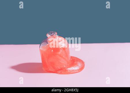 Aus dem Glasglas fließt pinker Schleim auf den pinken Tisch Stockfoto