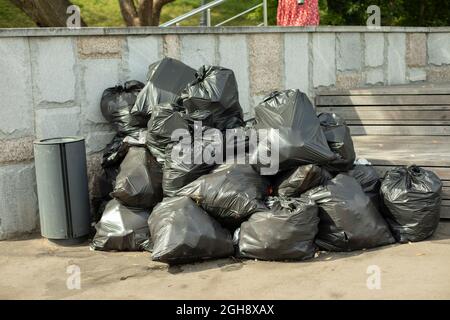 Müllsäcke auf der Straße. Schwarze Abfallbeutel. Plastiktüten mit Hausmüll im Park gesammelt. Viele Säcke stapeln sich im Müllhaufen. Stockfoto