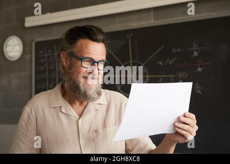 Nahaufnahme des Gesichts eines lächelnden Universitätsprofessors. Er hält einige Dokumente, eine Prüfung, ein Papier. Stockfoto