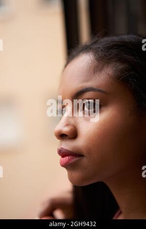 Vertikales Foto eines afroamerikanischen Mädchens, das sich aus dem Fenster lehnt. Dunkle Filmaufnahme. Stockfoto