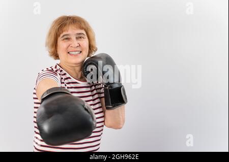 Ältere Frau in Kampfhandschuhen in einer defensiven Pose auf weißem Hintergrund. Stockfoto