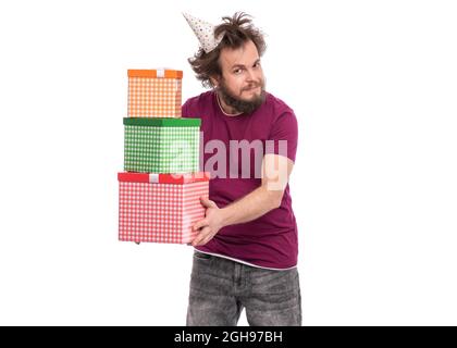 Verrückter bärtiger Mann mit witzigem Haarschnitt in Geburtstagskappe, isoliert auf weißem Hintergrund. Glücklicher Kerl mit Geschenkschachteln. Urlaubskonzept. Stockfoto