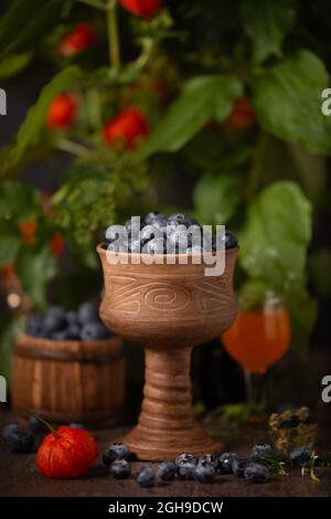 Heidelbeeren in einer Keramikschale vor einem Hintergrund von Blättern und Früchten der Physalis Stockfoto