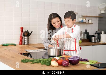 Mutter lehrt ihren Sohn, in der Küche Gemüse zu kochen. Lifestyle mit lateinischen Menschen. Kind lernt zu kochen. Stockfoto