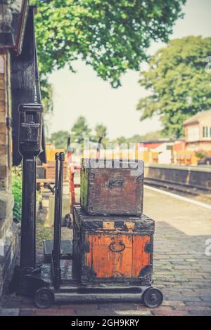 Nahaufnahme von alten Gepäcktaschen, die für den Transport und die Lieferung auf einer Dampfeisenbahnplattform bereit sind, zusammen mit einer Reihe von Gewichtswaagen. Stockfoto