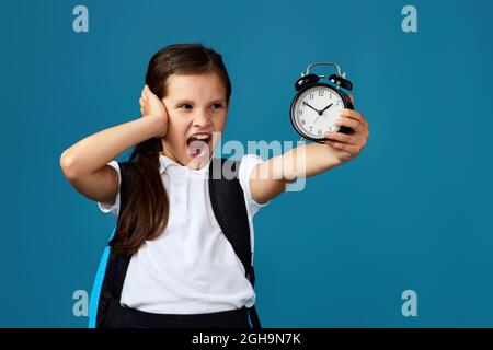 Schulmädchen mit Rucksack hält Wecker Stockfoto