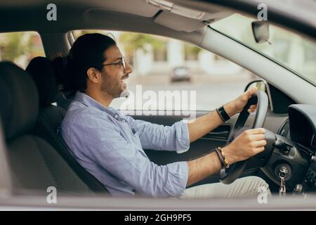 Hübscher inder, der Auto fährt, auf die Straße schaut und lächelt Stockfoto