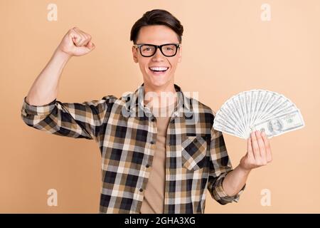 Foto von jungen lustigen Kerl halten Geld tragen karierte Hemd Brille isoliert auf beige Farbe Hintergrund Stockfoto
