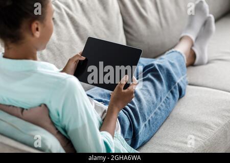 Jugendliche afroamerikanische Schülerin, die auf einem Tablet mit leerem Bildschirm tippt und zu Hause studiert Stockfoto