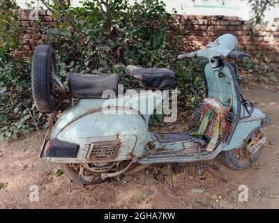 Nahaufnahme eines alten grauen Motorrollers, der neben einem schmutzigen, sonnigen Platz abgestellt wird Stockfoto